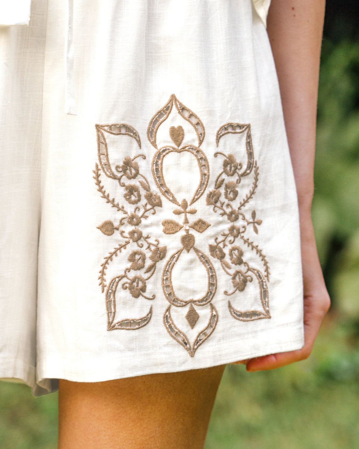 White fabric with gold embroidery held by a person outdoors